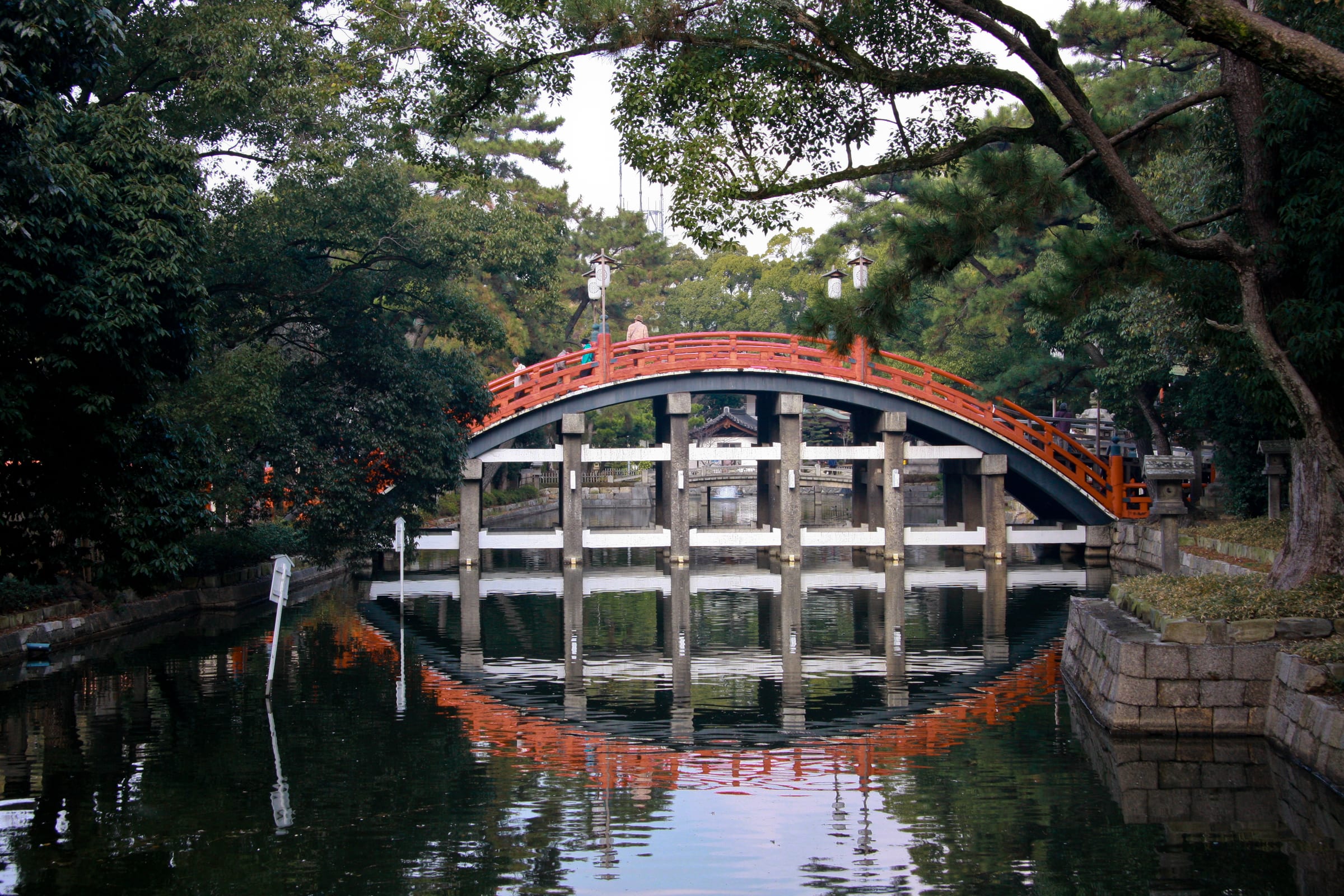 Red Japanese bridge reflected in calm garden water surrounded by greenery